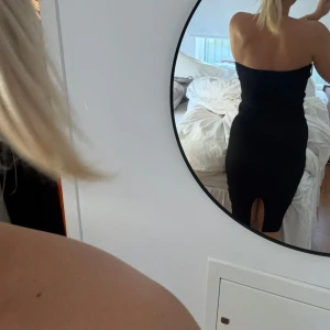 Svart ribbad axelbandslös klänning - Säljer en svart, ribbad klänning med axelbandslös design och slim passform. Klänningen är lång och har en snygg slits bak för extra edge. Perfekt för dig som gillar minimalistisk stil med en touch av attityd.