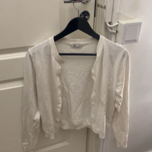 Vit kofta från Cubus  - Säljer en enkel och fräsch vit kofta från cubus. Den har rund hals, långa ärmar och knappar framtill. Perfekt att slänga över en topp när det är lite kyligt. Mjuk och skön bomullskvalitet som känns lätt mot huden.