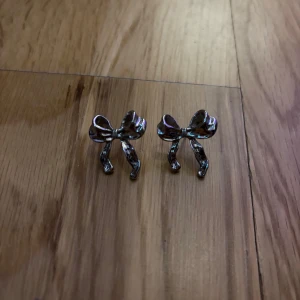 Söta silverörhängen med rosett - Ett par örhängen i form av glansiga rosetter i silverfärgat metall. De har en stilren och lekfull design som verkligen sticker ut. Perfekta för dig som gillar gulliga detaljer och vill addera lite extra till din look.