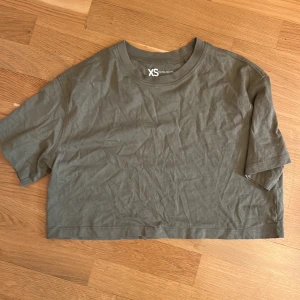 Olivgrön croppad t-shirt  - Enkel croppad t-shirt i olivgrönt från FSBN Sister. Modellen har korta ärmar, rund halsringning och är tillverkad i mjuk bomull🌸Perfekt till jeans eller shorts för en avslappnad look:)