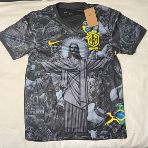 Brazil fotbollströja  - Snygg Brasilien fotbollströja från Nike med Dri-Fit material. Tröjan är svart med detaljer i gult och har ett unikt grafiskt tryck med Kristusstatyn och brasilianska motiv. Brasil-logga och Nike Swoosh på bröstet, samt flaggdetaljer på ärmarna. Perfekt för dig som vill sticka ut på planen.