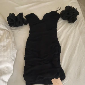 Svart klänning - Supersnygg svart kort klänning från SHEIN med offshoulder och stora volangärmar. Klänningen har en tight passform och är tillverkad i polyester. Perfekt för dig som vill sticka ut med en unik och trendig look.