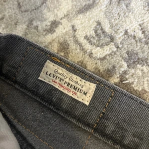 Levi's Premium grå jeans 501 straight - Säljer ett par Levi's Premium 501 jeans i mörkgrå färg. Klassisk straight fit med knappgylf och fem fickor. Jeansen har en enkel, clean look och är tillverkade i slitstarkt bomullsjeansmaterial. Perfekt för dig som gillar tidlös stil och vill ha ett par schyssta jeans.