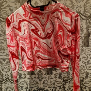 Rosa och vit swirlmönstrad långärmad topp - Säljer en riktigt cool långärmad topp med swirlmönster i rosa och vitt. Tröjan är croppad och har en slim passform som sitter snyggt. Perfekt för dig som gillar att sticka ut med färg och mönster. Materialet är mjukt och stretchigt, vilket gör den skön att bära.