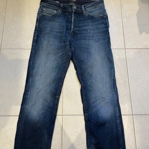 Mörkblå jeans från Jack & Jones - Snygga mörkblå jeans från Jack & Jones med klassisk femficksdesign och raka ben. Jeansen har en lätt tvättad look med subtila slitningar och kontrastsömmar. Passar dig som gillar en enkel och stilren vibe. Materialet är robust denim i bomull.