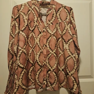 Rutig långärmad skjorta från Marta - Snygg långärmad skjorta från Marta i storlek S med unikt rutig mönster i beige och bruna toner. Skjortan har knappar framtill, rynkad krage och smockade ärmslut som ger en cool och trendig vibe. Perfekt för dig som gillar statement-plagg och vill sticka ut.