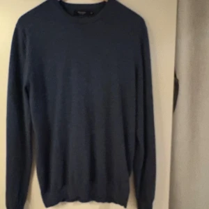 Blå merinoulltröja från Matinique - Säljer en stilren blå tröja från Matinique i 100% merinoull. Tröjan har rund hals, lång ärm och ribbade muddar vid hals, ärmslut och nederkant. Perfekt för dig som gillar klassisk och enkel design med mjukt material.