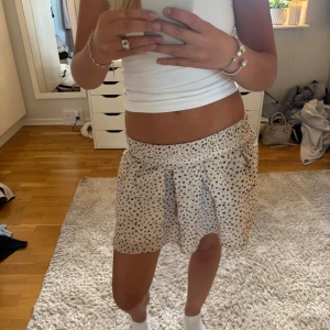 Prickig beige kortkjol  - Säljer en söt beige kortkjol med svarta prickar och bred resår i midjan. Kjolen är i barnstorlek men sitter som s/xs💕(kjolen är nervikt på bilden)💕