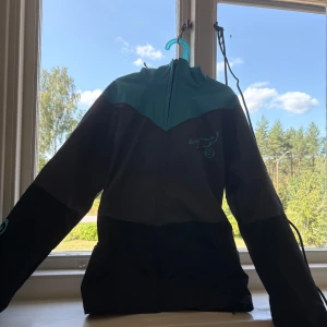 Hundförarjacka - Snygg hundförarjacka från D4M i grått och blått med broderad Dogs4me-logga på bröstet. Jackan har huva, dragkedja framtill och praktiska fickor. Perfekt för dig som är hundförare eller bara tränar hund! NYPRIS: 1000kr ALDRIG ANVÄND