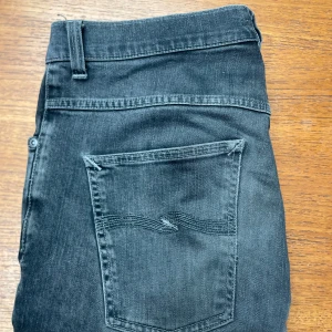 Nudie Jeans - Snygga svarta jeans från Nudie Jeans Co i klassisk femficksmodell. Jeansen har raka ben och coola detaljer på bakfickorna med Nudie-signaturen. Materialet är slitstarkt denim i bomull och passformen är normal. Perfekt för dig som gillar stilrena och tidlösa jeans.