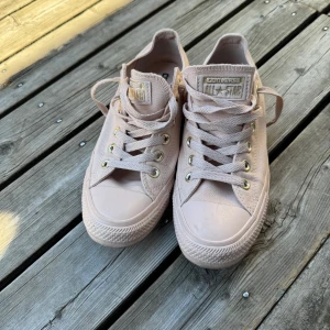 Ljusrosa Converse All Star sneakers - Säljer ett par ljusrosa Converse All Star sneakers i klassisk låg modell. Skorna har rund tå, platt sula och snörning med metallöglor. Ovandelen är i textil och yttersulan i gummi. Perfekt för dig som gillar stilrena och softa färger.