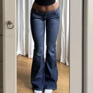 Blå bootcut jeans låg midja - Snygga blå jeans med bootcut passform och låg midja. Jeansen har klassisk femficksdesign och är gjorda i ett slitstarkt denimtyg. Perfekta för dig som gillar retrovibbar och vill ha en cool siluett med utsvängda ben.