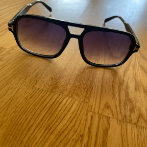 Svarta Tom Ford solglasögon - Säljer ett par svarta Tom Ford solglasögon med fyrkantig-ish form och guldig T-båge. Dem har en oversised passform. Originalförpackningen är borta därmed saknas äkthetsbevis. Endast använd ett fåtal gånger. Skriv gärna vid övriga frågor!