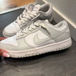 Nike Dunk Low sneakers i vitt - Nike Dunk Low sneakers i fräsch vit färg med ljusgrå detaljer. Fick i födelsedagspresent förra året, har använd ungefär 3 gårnger. Är som nya, (nypris 1500 säljer för 1100 pris kan diskuteras)