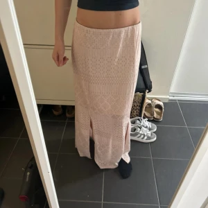 Ljusrosa långkjol från Xhilaration - Supersöt ljusrosa långkjol från Xhilaration med diskret mönster och två slitsar framtill. Kjolen har en svart elastisk midja och är gjord i ett mjukt syntetmaterial som känns skönt mot huden. Perfekt för dig som gillar en chill och feminin stil. Jag har vanligtvis xs o den sitter så på mig så jag tror den krymt lite 