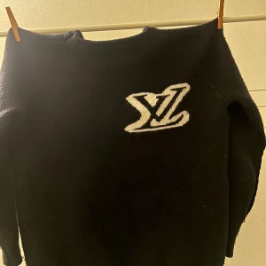 Svart stickad tröja Louis Vuitton - PRIS GÅR ATT DISKUTERA.                               Svart stickad tröja från Louis Vuitton med stor vit LV-logga på bröstet. Rund hals och långa ärmar, mjuk och skön känsla. Perfekt för dig som gillar exklusiva märken och vill ha en clean look med tydlig logga.