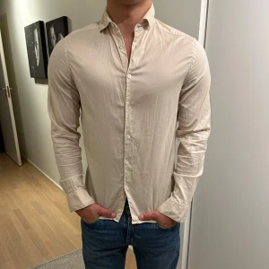 J Lindberg skjorta - En snygg skjorta från J Lindberg i en unik färg som är en blandning mellan beige och gul. Tröjan är använd men inga defekter. Nypris är ca 600kr. Hör av er vid frågor eller funderingar 