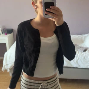 Svart kofta med knappar - Svart kofta med rund hals och knäppning framtill. Långärmad och i mjukt material som passar perfekt till lager-på-lager. Enkel och stilren design som funkar till många olika outfits.