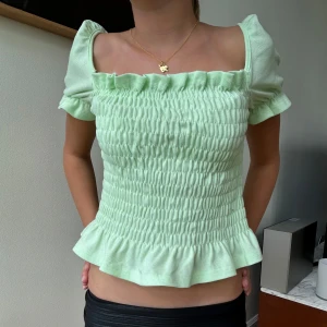 Ljusgrön blus med volang - Supersöt ljusgrön blus med smockad kropp, puffiga korta ärmar och volangkant nertill. Skit snygg till en fest eller till ett bar jeans till vardagen! Modellen bär storlek S men är själv en xs!