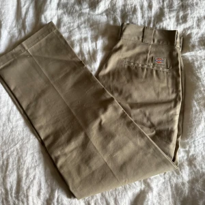 Dickies 874 Original Fit chinos - Säljer ett par klassiska Dickies 874 Original Fit byxor i beige. De har rak passform, normal midja och är tillverkade i slitstark bomull/polyester-mix. Typisk Dickies-logga baktill och pressveck längs benen för en clean look. Perfekta för dig som gillar streetwear och workwear.