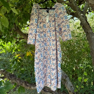 Blommig långklänning från Lindex - Säljer en ljus långklänning från Lindex med blommigt mönster i blått och brunt. Klänningen har trekvartsärm och rund halsringning. Tillverkad i mjuk bomull, perfekt för varma dagar. Snygg och flowy passform som ger en chill vibe. Storlek L. Helt ny med tags/ prislapp fortfarande kvar. 
