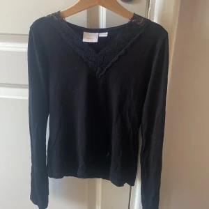Svart långärmad topp med spets Gina Tricot - Svart långärmad topp från Gina Tricot med snygg spetsdetalj i v-ringning. Mjuk bomullskänsla och stilren design som funkar till många looks. Spetsen ger en extra touch och gör toppen lite mer unik. Perfekt för dig som gillar enkla men fina detaljer.