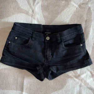 Low waisted jeansshorts från KappAhl - Snygga svarta low waisted jeansshorts från KappAhl med klassisk femficksdesign, knapp och dragkedja framtill samt uppvikta benslut. Shortsen har bälteshällor och är gjorda i mjukt denimtyg som sitter skönt. Perfekta för varma dagar och chill häng.
