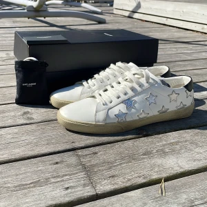 Saint Laurent vita sneakers med stjärnor - Säljer dessa tvär feta saint Laurent skor i storlek 44. De är i ett otroligt bra skick. Lite smutsiga där nere på det bruna av skon men går enkelt att ta bort med rätt medel. Syns även inte så mycket. Box✅nya snören✅Saint Laurent kort✅ kommer med på köpet. Hör av dig vid funderingar.🙌