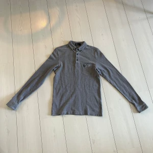 Fred Perry Piké - En grå långärmad piké av märket Fred Perry. Tröjan är i mycket bra skick och har inga defekter. Hör gärna av dig vid eventuella frågor!