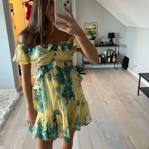 Blommig klänning - Superfin gul kortklänning med grönt blommigt mönster och volangdetaljer och som är öppen på sidorna😍