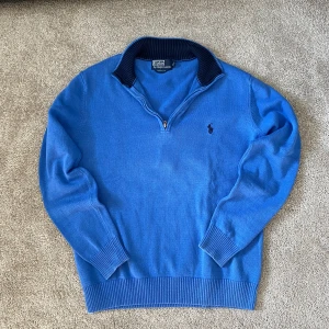 Blå half zip tröja från Polo Ralph Lauren - Säljer en klassisk blå tröja från Polo Ralph Lauren med half zip och ribbad mörkblå krage. Tröjan har lång ärm, broderad logga på bröstet och är gjord i mjuk bomull. Perfekt för dig som gillar stilren och sportig look. Liten i stoltek dvs passar S