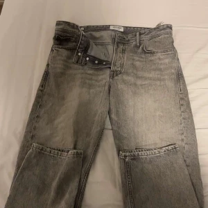 Grå loose fit jeans från Jack & Jones - Säljer ett par grå jeans från Jack & Jones i loose fit-modellen Chris. Jeansen har raka ben, klassisk femficksdesign och snygg tvättad look. Passar dig som gillar avslappnad stil och bredare siluett. Materialet är slitstarkt denim och midjan är normal.