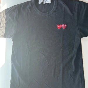 Svart Comme des Garçons Play t-shirt - Svart t-shirt från Comme des Garçons Play med två röda hjärtan med ögon broderade på bröstet. Klassisk rund hals och korta ärmar. Tillverkad i mjuk bomull som är skön mot huden.