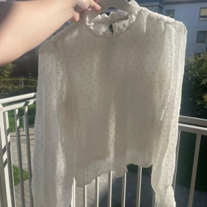 Vit prickig blus med volangkrage - Supersöt vit blus från nelly med små prickar, volangdetaljer vid halsen och långärmade puffiga ärmar. Blusen har en lätt transparent känsla och knäppning i nacken. Perfekt för dig som gillar romantisk och trendig stil. Strl 34. Använd och har försökt och tvätta bort ljusa gula fläckar från svett och det mesta ska vara borta och inget man ser när man har på sig den och har även tagit kort vid armhålorna så ni ser hur det ser ut där. Går att pruta 