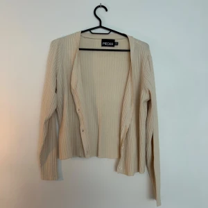 Beige ribbad kofta från Pieces - Snygg beige kofta från Pieces med ribbad struktur och knappar framtill. Perfekt att ha över klänning. 