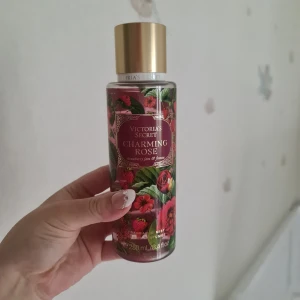 Victoria's Secret Charming Rose mist - Fräsch body mist från Victoria's Secret i doften Charming Rose. Flaskan är dekorerad med röda rosor och jordgubbar, har guldig kork och rymmer 250 ml. Doften har inslag av ros, jordgubbssylt och fresia. Perfekt för dig som gillar blommiga och söta toner. Helt ny och oanvänd