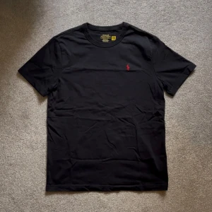 Ralph Lauren T-shirt Svart - Säljer en snygg svart T-shirt med rött märke från Ralph Lauren, Skick: 10/10 knappt använd. Storlek S, hör gärna av er vid frågor, Mvh