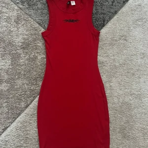 Röd tight kortklänning Divided H&M - Säljer en röd tight kortklänning från Divided H&M i storlek XXS. Klänningen är ärmlös med rund halsringning och har en svart tribal-detalj framtill. Perfekt för dig som gillar en enkel men edgy look.