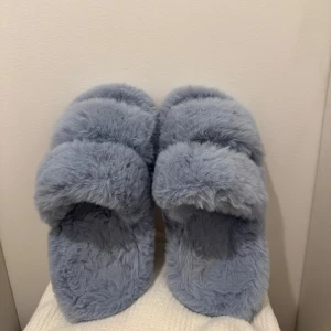 Ljusblå fluffiga tofflor - Supermjuka och fluffiga ljusblå tofflor med öppen tå och bred rem över foten. Perfekta att gå runder i hemmet med! Osäker på vart dom är köpta men tror hunke möller💙
