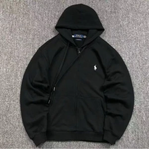 Svart hoodie från Polo Ralph Lauren - Svart hoodie från Polo Ralph Lauren med dragkedja och klassisk huva. Tröjan har en vit broderad logga på bröstet, känguruficka och ribbade muddar. Perfekt för dig som gillar en clean och stilren look.