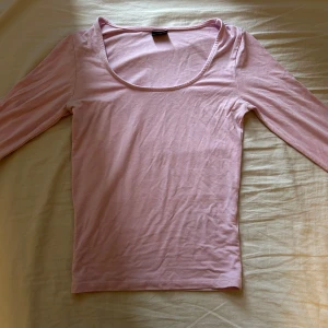 Ljusrosa långärmad topp Gina Tricot - Supersöt ljusrosa långärmad topp från Gina Tricot i mjuk bomull. Modellen har en djup, rundad urringning och smal passform som sitter snyggt. Slits på armen. Perfekt att styla med jeans eller kjol för en fräsch look.