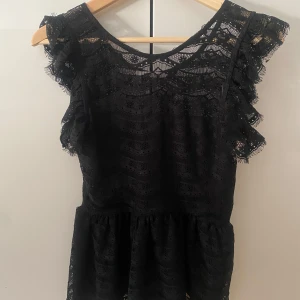 Svart spetstopp med volang - Vacker och elegant topp från Gina tricot. Den har volanger och spets. Helt öppen spets på ryggen. Perfekt som festtopp.