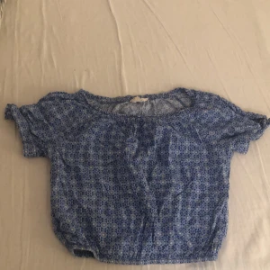 Blå blommig blus med resår - Söt blå blus med småblommigt mönster och resår i både midja och ärmslut. Modellen är croppad och har korta ärmar samt rund halsringning. Perfekt för dig som gillar en avslappnad och somrig stil.