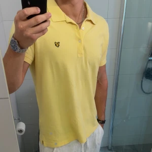Gul pikétröja från Lyle & Scott - Snygg gul pikétröja från Lyle & Scott🦅Klassisk krage, två knappar och örnlogga på bröstet. Tröjan är i bomull och har korta ärmar, perfekt för en fräsch och avslappnad stil under varma dagar☀️