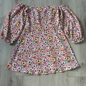 Blommig kortklänning från H&M Divided - Supersöt kortklänning med puffärmar från H&M Divided. Klänningen har ett färgglatt blommönster i rosa, gul, vit och svart på en ribbad bomullsmix. Offshoulder-modell med smock upptill och voluminösa ärmar. Perfekt för sommarens alla tillfällen!