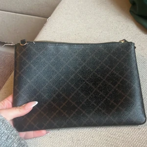 Brun kuvertväska med rutigt mönster - Snygg brun kuvertväska i skinnimitation med diskret rutigt mönster och dragkedja upptill. Perfekt storlek för mobilen och det viktigaste. Enkel och stilren design som passar till många outfits.