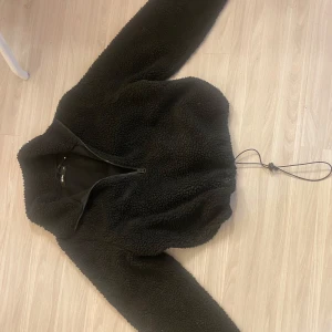 Svart teddyjacka från Bik Bok XS - Mysig svart teddyjacka från Bik Bok i storlek XS. Jackan har dragkedja framtill, hög krage och justerbar dragsko nertill. Perfekt för kyliga dagar när du vill vara både varm och snygg. Långärmad och fluffig med en loose fit.