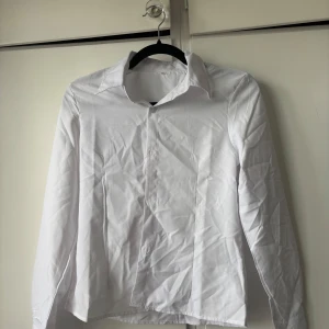 Vit klassisk skjorta med krage - Vit skjorta i storlek S – klassisk modell i nyskick, endast provad. Skrynklig på bild men jag fixar det självklart innan den skickas! Skjortan har knäppning framtill och är tillverkad i ett lätt bomullstyg. Perfekt för dig som gillar en clean och enkel look. 