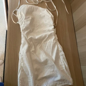 Vit kort klänning i linnemix  - Supersöt vit kort klänning från Bershka i storlek XS. Klänningen har tunna axelband, öppen rygg med snörning och en liten slits på sidan. I linnemix🤍🤍🤍.