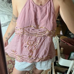 Rosa vintage topp  - Supersöt rosa halterneck linnetopp med broderade blommor och guldiga paljettdetaljer. Toppen har öppen rygg och knyt i nacken och bak, vilket ger en luftig och somrig känsla. Perfekt för dig som gillar unika detaljer och boho-vibe. Står ingen storlek men jag som har S kan ha den! Jättefin topp verkligen🥰👏🏼